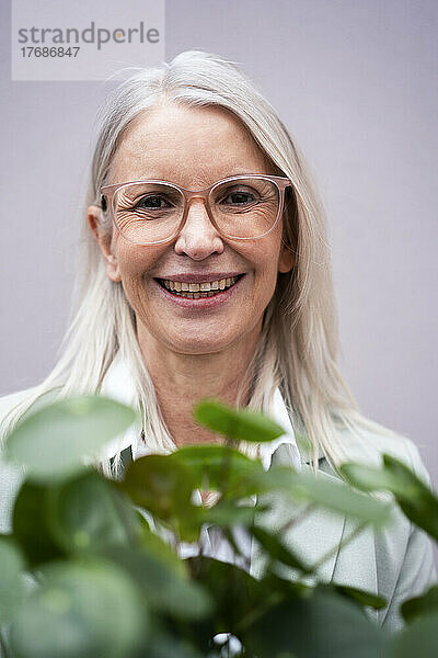 Ältere Geschäftsfrau lächelt neben Pflanzen