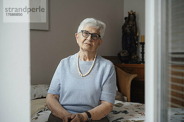 Einsame ältere Frau sitzt zu Hause im Schlafzimmer auf dem Bett