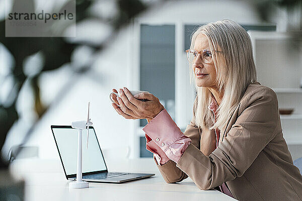 Ältere Geschäftsfrau hält Kaffeetasse am Schreibtisch im Büro