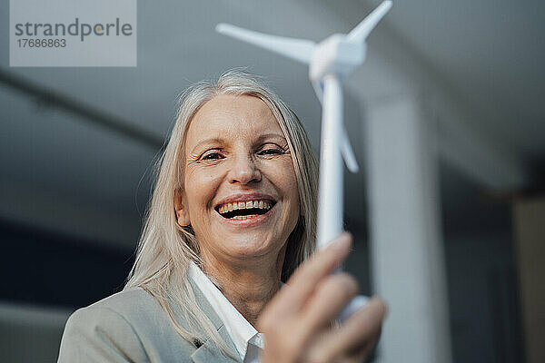 Glückliche Geschäftsfrau hält Windturbinenmodell im Büro