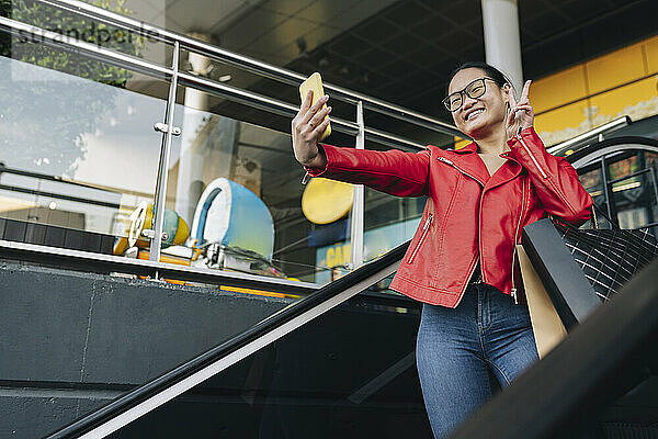 Lächelnde Frau macht ein Selfie mit ihrem Smartphone auf der Rolltreppe