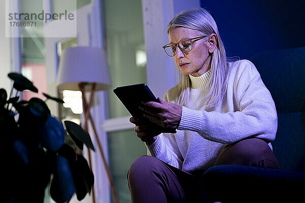 Ältere Frau sitzt zu Hause und benutzt Tablet-PC