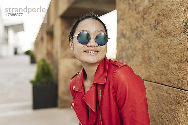 Smiling woman wearing sunglasses in front of brown wall