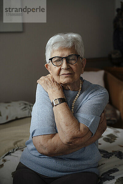 Ältere Frau mit geschlossenen Augen umarmt sich zu Hause im Bett
