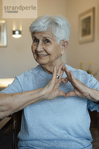 Glückliche ältere Frau  die zu Hause ein Herzzeichen mit den Händen macht