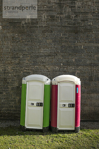 Zwei tragbare Toiletten stehen nebeneinander vor einer Ziegelwand