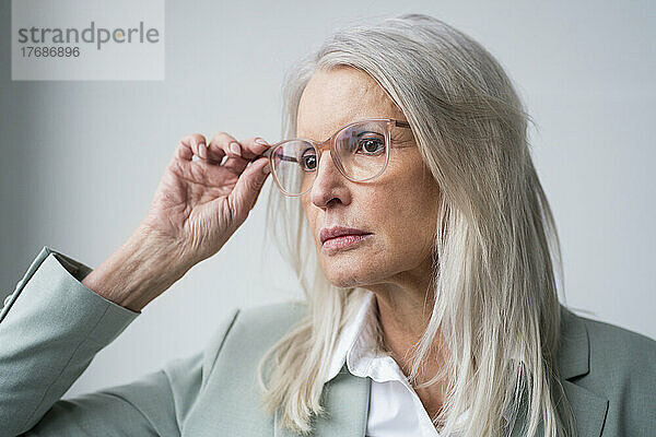 Besorgte Geschäftsfrau hält Brille vor weißem Hintergrund