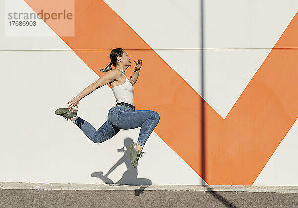 Junge Frau springt auf Fußweg vor Mauer