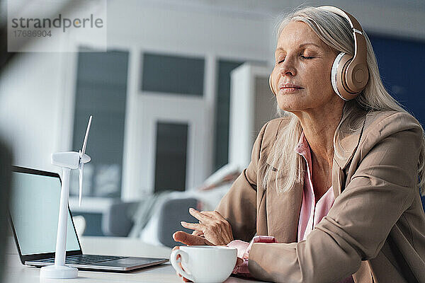 Geschäftsfrau mit geschlossenen Augen hört im Büro Musik über Kopfhörer