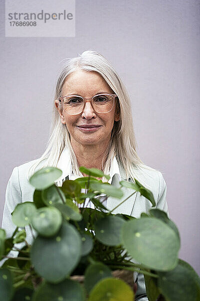 Lächelnde Geschäftsfrau bei Pflanzen vor der Wand