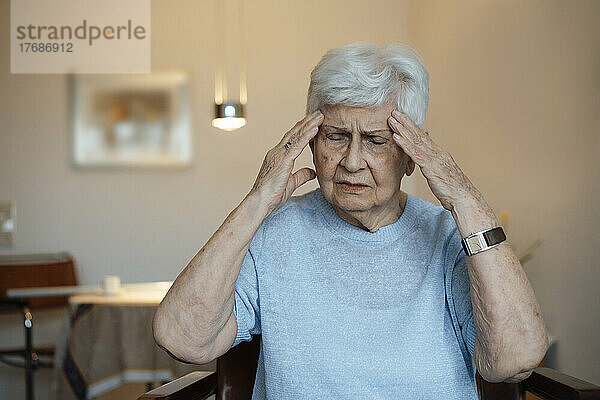Müde ältere Frau kämpft zu Hause mit Kopfschmerzen