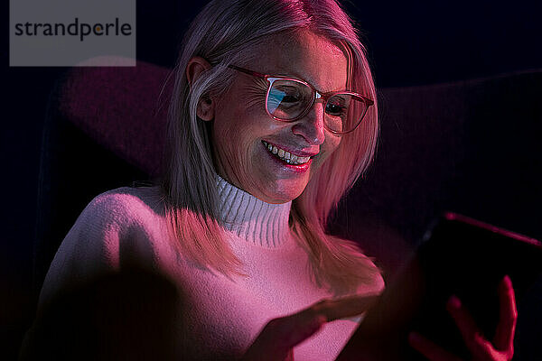 Lächelnde ältere Frau benutzt Tablet-PC in der Dunkelkammer