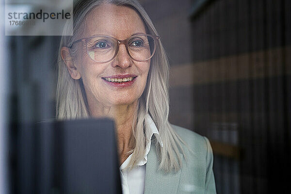 Nachdenkliche Geschäftsfrau mit Brille durch Glas gesehen