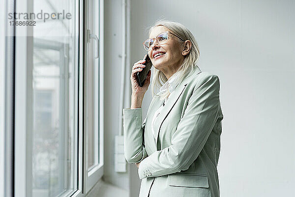 Ältere Geschäftsfrau spricht mit Smartphone am Fenster im Büro