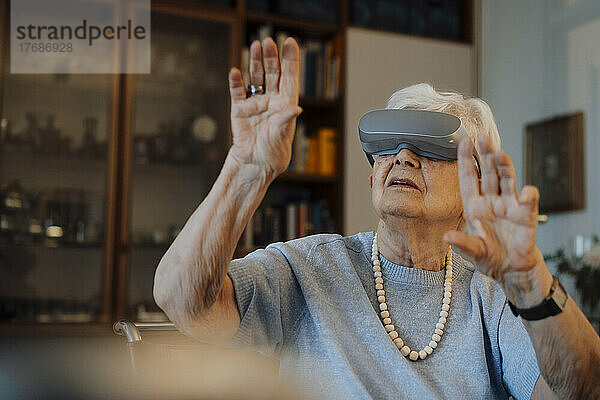 Ältere Frau mit Virtual-Reality-Simulator gestikuliert zu Hause