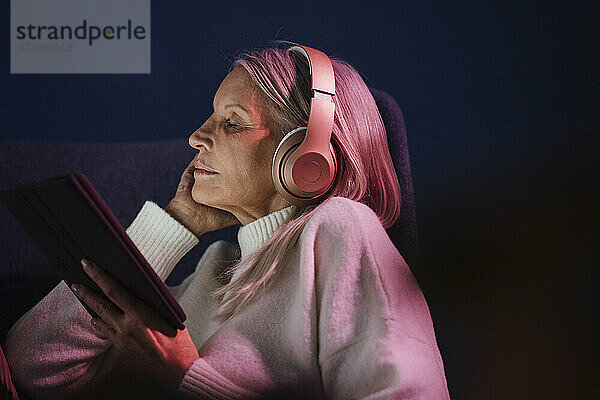 Ältere Frau hält Tablet-PC und hört Musik über Kopfhörer