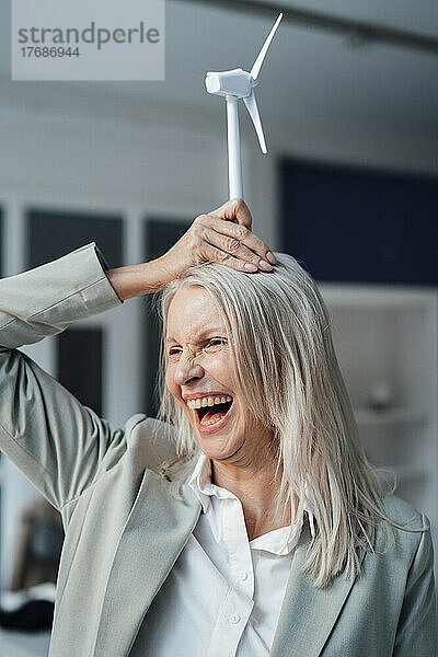 Verspielte Geschäftsfrau hält im Büro ein Windturbinenmodell über sich