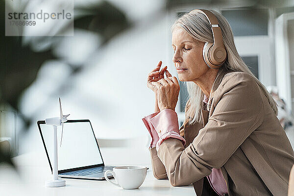 Geschäftsfrau hört Musik mit geschlossenen Augen am Schreibtisch im Büro