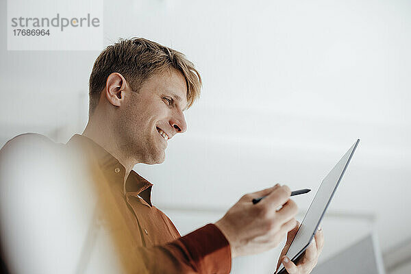 Lächelnder Geschäftsmann mit digitalisiertem Stift und Blick auf den Tablet-PC im Büro
