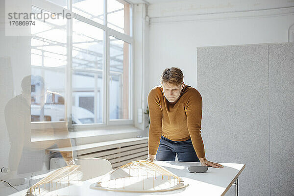 Architekt betrachtet blattförmiges Modell  das im Büro auf dem Schreibtisch lehnt