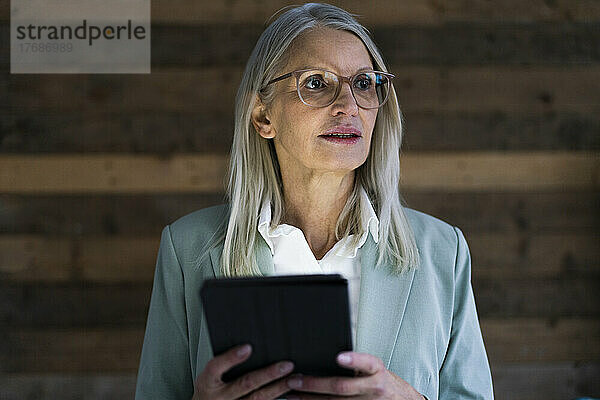 Nachdenkliche Geschäftsfrau hält Tablet-PC vor der Wand