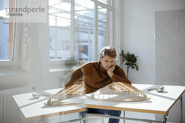 Architekt sitzt mit dem Kopf in der Hand und betrachtet das blattförmige Modell im Büro