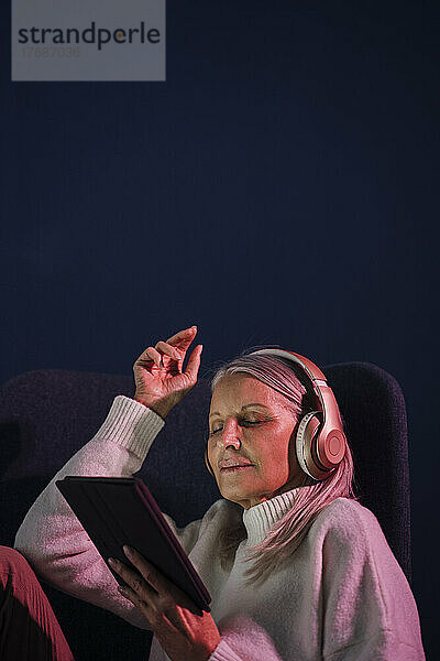 Ältere Frau genießt Musik über kabellose Kopfhörer vor blauem Hintergrund