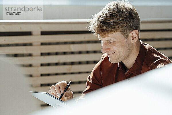 Lächelnder Geschäftsmann mit digitalisiertem Stift und Tablet-PC im Büro