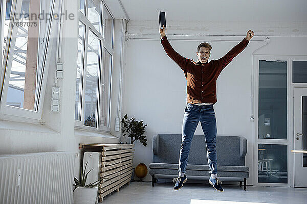 Happy businessman with tablet PC jumping in office