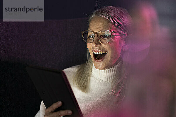 Lachende ältere Frau blickt auf Tablet-PC