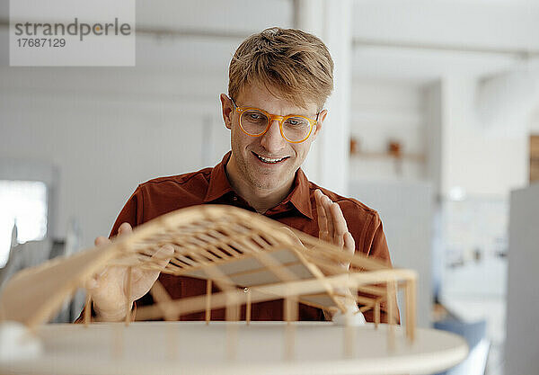 Lächelnder Architekt mit Brille blickt auf blattförmiges Modell im Büro