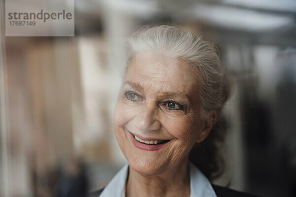 Glückliche ältere Geschäftsfrau mit grauem Haar  die durch das Fenster schaut