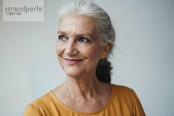 Lächelnde ältere Frau mit grauen Haaren vor weißem Hintergrund