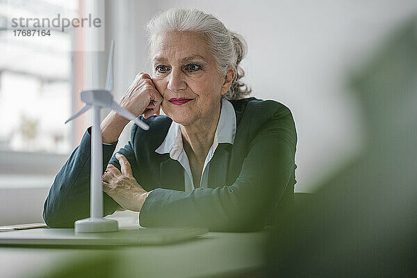 Geschäftsfrau betrachtet Windturbinenmodell am Schreibtisch im Büro