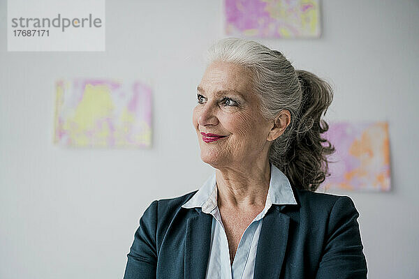Lächelnde Geschäftsfrau mit grauen Haaren  die vor der Wand steht