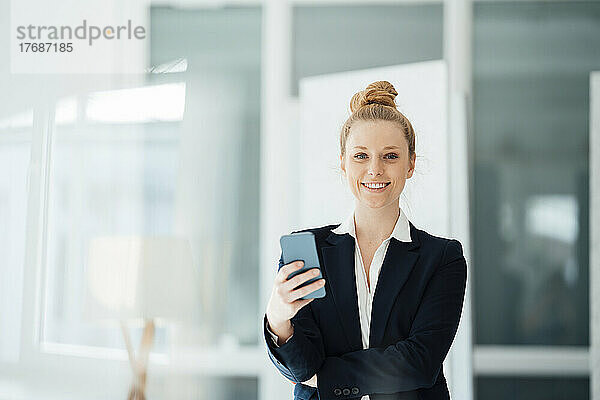 Geschäftsfrau mit Haarknoten hält Smartphone im Büro