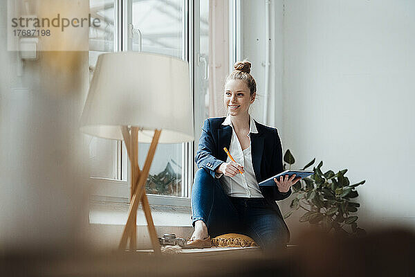 Nachdenkliche Geschäftsfrau mit Tablet-PC sitzt am Fenster im Büro