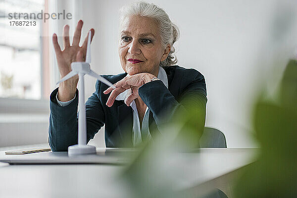 Ältere Geschäftsfrau mit Windturbinenmodell sitzt am Schreibtisch im Büro