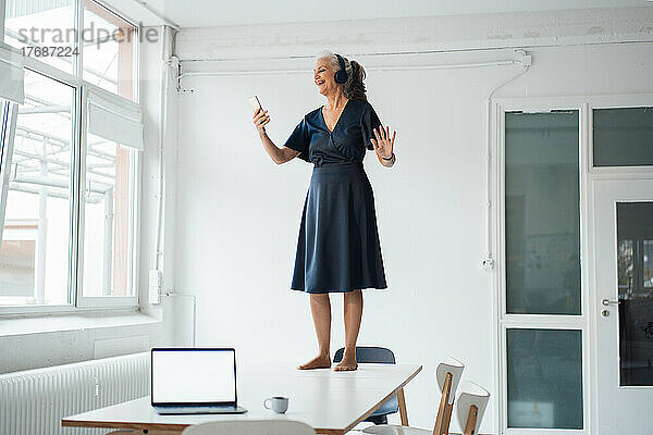 Glückliche Geschäftsfrau mit Smartphone am Schreibtisch im Büro