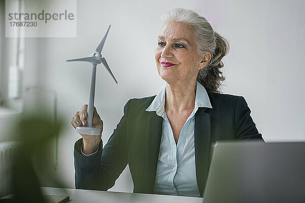 Geschäftsfrau mit Windturbinenmodell sitzt am Schreibtisch im Büro