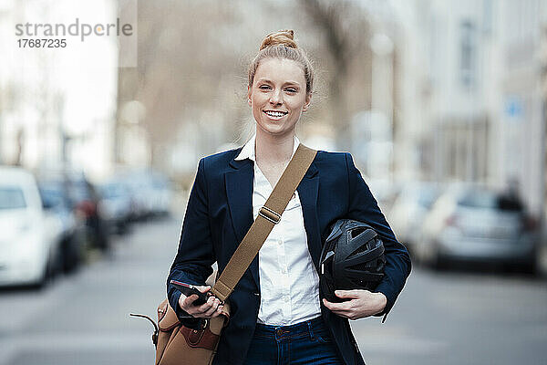 Lächelnde Geschäftsfrau mit Helm und Smartphone