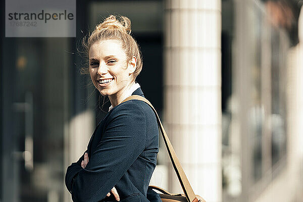 Lächelnde Geschäftsfrau vor dem Büro an einem sonnigen Tag