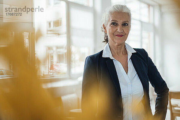 Lächelnde Geschäftsfrau mit grauen Haaren  die im Büro steht