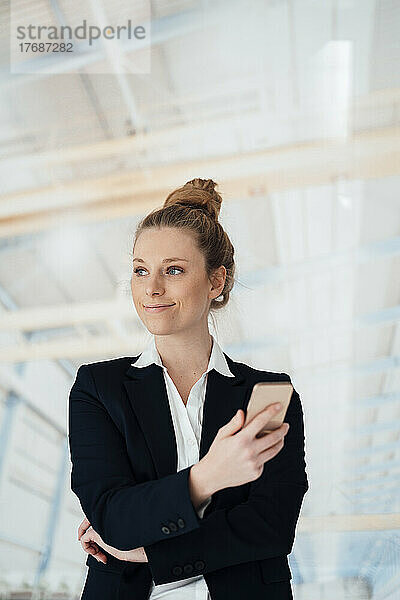 Lächelnde Geschäftsfrau hält Smartphone in der Fabrik