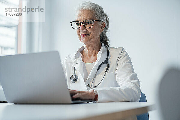 Arzt mit Brille und Laptop am Schreibtisch
