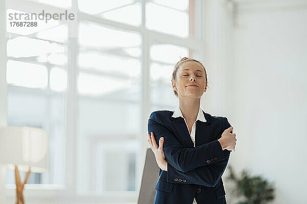Geschäftsfrau mit geschlossenen Augen umarmt sich im Büro
