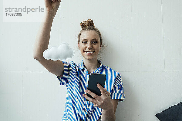 Lächelnde Geschäftsfrau mit Smartphone und ausgeschnittener Wolke vor der Wand