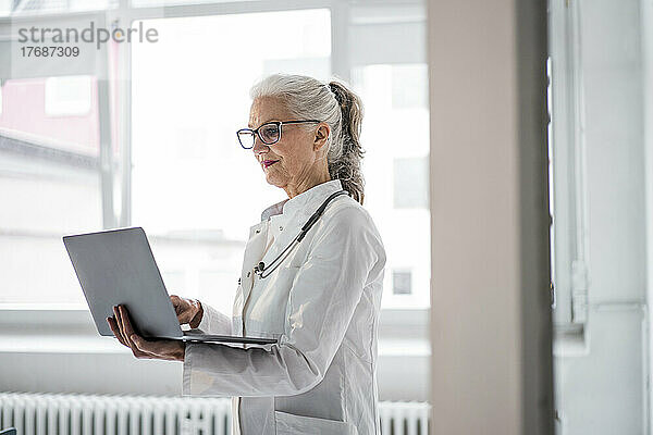 Arzt mit Brille und Laptop am Fenster