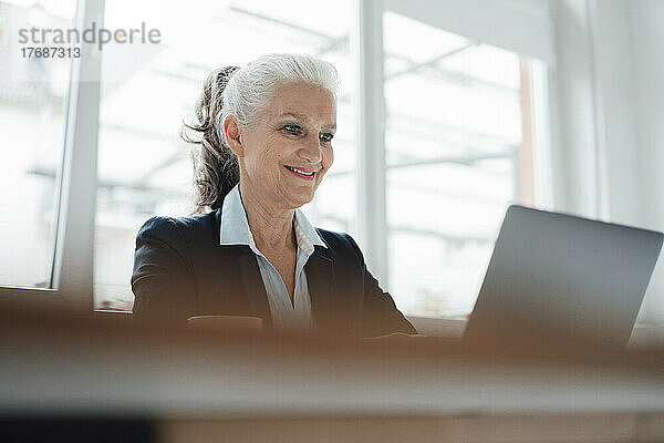 Glückliche ältere Geschäftsfrau  die am Laptop am Schreibtisch im Büro arbeitet