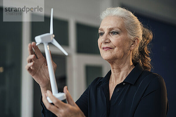 Lächelnde Geschäftsfrau untersucht Windturbinenmodell im Büro